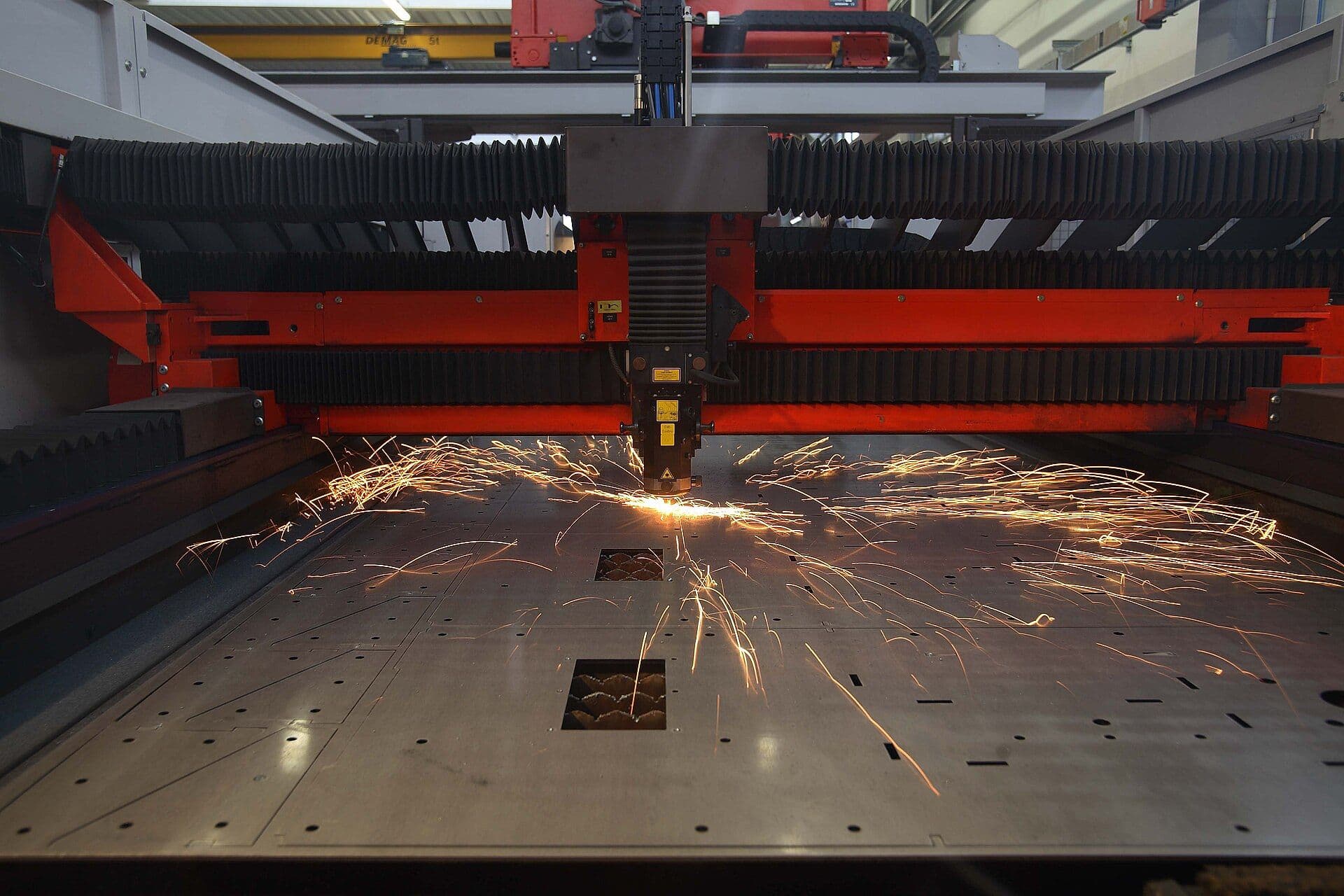CNC fiber laser cutting head profiling a steel sheet, sparks streaming across the bed